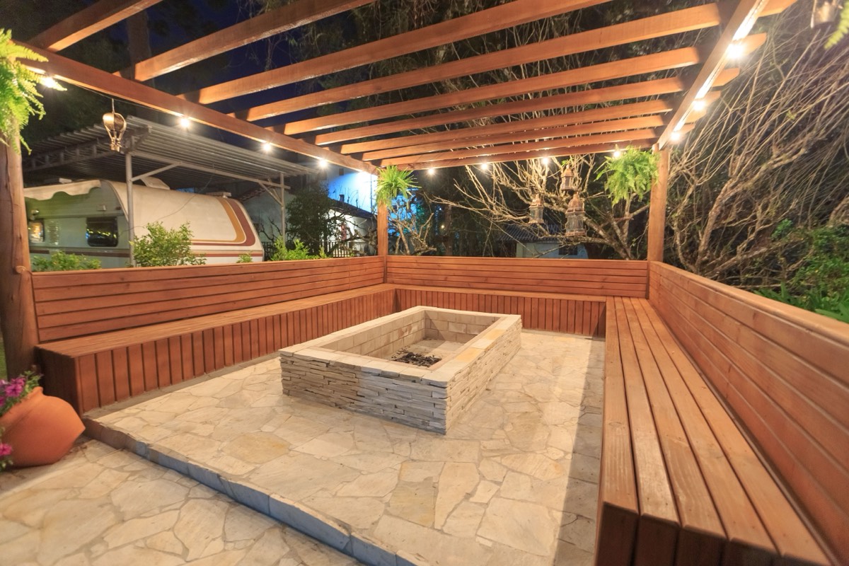 A lit pergola over a stone patio, with built-in bench seating around a fire pit.